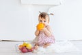 A little girl is sitting in a bright room with a plate of fruit and eating an orange Royalty Free Stock Photo