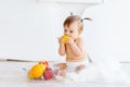 A little girl is sitting in a bright room with a plate of fruit and eating a pear Royalty Free Stock Photo