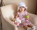 Little girl sitting on a chair in a white hat and a dress in a print with an apple Royalty Free Stock Photo