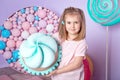 Little girl sitting in colorful room around big toyful candies, donut, lollipop Royalty Free Stock Photo