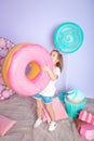 Little girl sitting in colorful room around big toyful candies, donut, lollipop Royalty Free Stock Photo