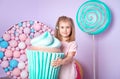 Little girl sitting in colorful room around big toyful candies, donut, lollipop Royalty Free Stock Photo