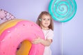 Little girl sitting in colorful room around big toyful candies, donut, lollipop Royalty Free Stock Photo