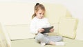 A little girl is sitting on the couch in the living room and holding a tablet in her hands. in the interior Royalty Free Stock Photo