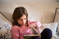 A little girl sitting on a couch and reading a book. Royalty Free Stock Photo