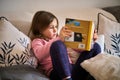 A little girl sitting on a couch and reading a book. Royalty Free Stock Photo