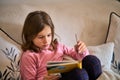 A little girl sitting on a couch and reading a book. Royalty Free Stock Photo