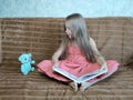 A little girl is sitting on the couch and reading a book to her teddy bear Royalty Free Stock Photo