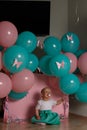 little girl sitting on the floor in the room next to the balloons, first birthday, celebrate. one year old blue and pink balls wit Royalty Free Stock Photo