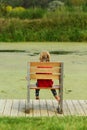 Little girl sitting in a giant wooden chair on the lake bank