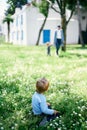 Little girl sitting on green grass and looking at people walking by Royalty Free Stock Photo