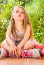 Little girl sitting on ground wearing her roller skates and crossing her legs looking the sky, in a garden background Royalty Free Stock Photo