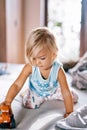 Little girl sitting on her knees on the bed with a toy tractor Royalty Free Stock Photo