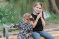 Little girl sitting with her small sister on bench in summer spring park and talking on smartphone Royalty Free Stock Photo