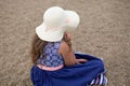 Little girl sitting, holding summer hat and beautiful blue dress on the beach Royalty Free Stock Photo