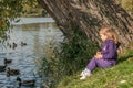 A little girl sitting on a lake side and feeding ducks Royalty Free Stock Photo