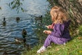 A little girl sitting on a lake side and feeding ducks Royalty Free Stock Photo