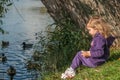 A little girl sitting on a lake side and feeding ducks Royalty Free Stock Photo