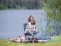 Little girl sitting near campfire. Girl roasting bread over campfire