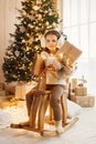 Little girl sitting near Christmas tree on a wooden rocking horse toy Royalty Free Stock Photo