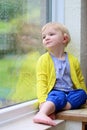 Little girl sitting next window on rainy day Royalty Free Stock Photo