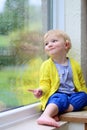 Little girl sitting next window on rainy day Royalty Free Stock Photo