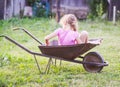 Little girl sitting in the old iron wheelbarrow in the village at summer Royalty Free Stock Photo