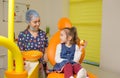 a little girl is sitting in an orange dental chair, smiling with a red apple in her hands. Pediatric dentistry, baby