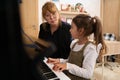 Little girl sitting at piano near her teacher pianist musician, learning music during individual music lesson at home