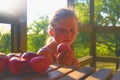 Little girl is sitting on porch in summer. Small girl is eating apples. Apples on table. Dreamy and romantic image