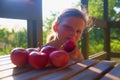 Little girl is sitting on porch in summer. Small girl is eating apples. Apples on table. Dreamy and romantic image