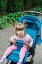 Little girl is sitting in a pram in a beautiful park. Royalty Free Stock Photo