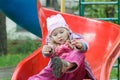 Little girl sitting on red plastic playground slide and tying shoelaces of her kids trainers