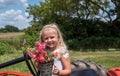 Little girl sitting on a tractor holding a bouquet of flowers Royalty Free Stock Photo