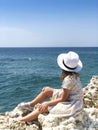 Little girl sitting on rocky shore while looking at sea during summer vacation with family on seaside Royalty Free Stock Photo