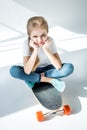 Little girl sitting on skateboard with crossed legs Royalty Free Stock Photo