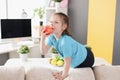 Little girl sitting on sofa and eating red apple at home Royalty Free Stock Photo