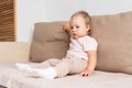 Little girl sitting on sofa and looking away with interest. Blond blue-eyed baby in light clothes Royalty Free Stock Photo