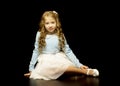 A little girl is sitting in the studio on the floor on a black b Royalty Free Stock Photo