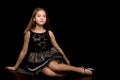 A little girl is sitting in the studio on the floor on a black background. Royalty Free Stock Photo