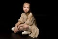 A little girl is sitting in the studio on the floor on a black background. Royalty Free Stock Photo