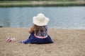 Little girl sitting in summer hat and beautiful dress on the beach Royalty Free Stock Photo