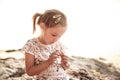 Little girl sitting on a sunlit beach at sunset, playing