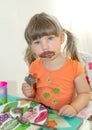 A little girl is sitting at a table and eating chocolate ice cream. Her face was dirty in chocolate.