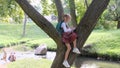 a little girl sitting on a tree branch in the park or in the backyard and drawing in a notebook. An introverted child