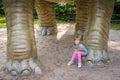 Little girl sitting under huge Diplodocus dinosaur sculpture