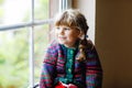 Little girl sitting by window. Preschool child wear cozy self knitted wool sweater. Toddler watching on rain outside Royalty Free Stock Photo