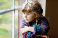 Little girl sitting by window. Preschool child wear cozy self knitted wool sweater. Toddler watching on rain outside Royalty Free Stock Photo