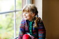 Little girl sitting by window. Preschool child wear cozy self knitted wool sweater. Toddler watching on rain outside Royalty Free Stock Photo