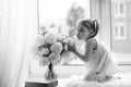 A little girl is sitting on the windowsill. A bouquet of flowers